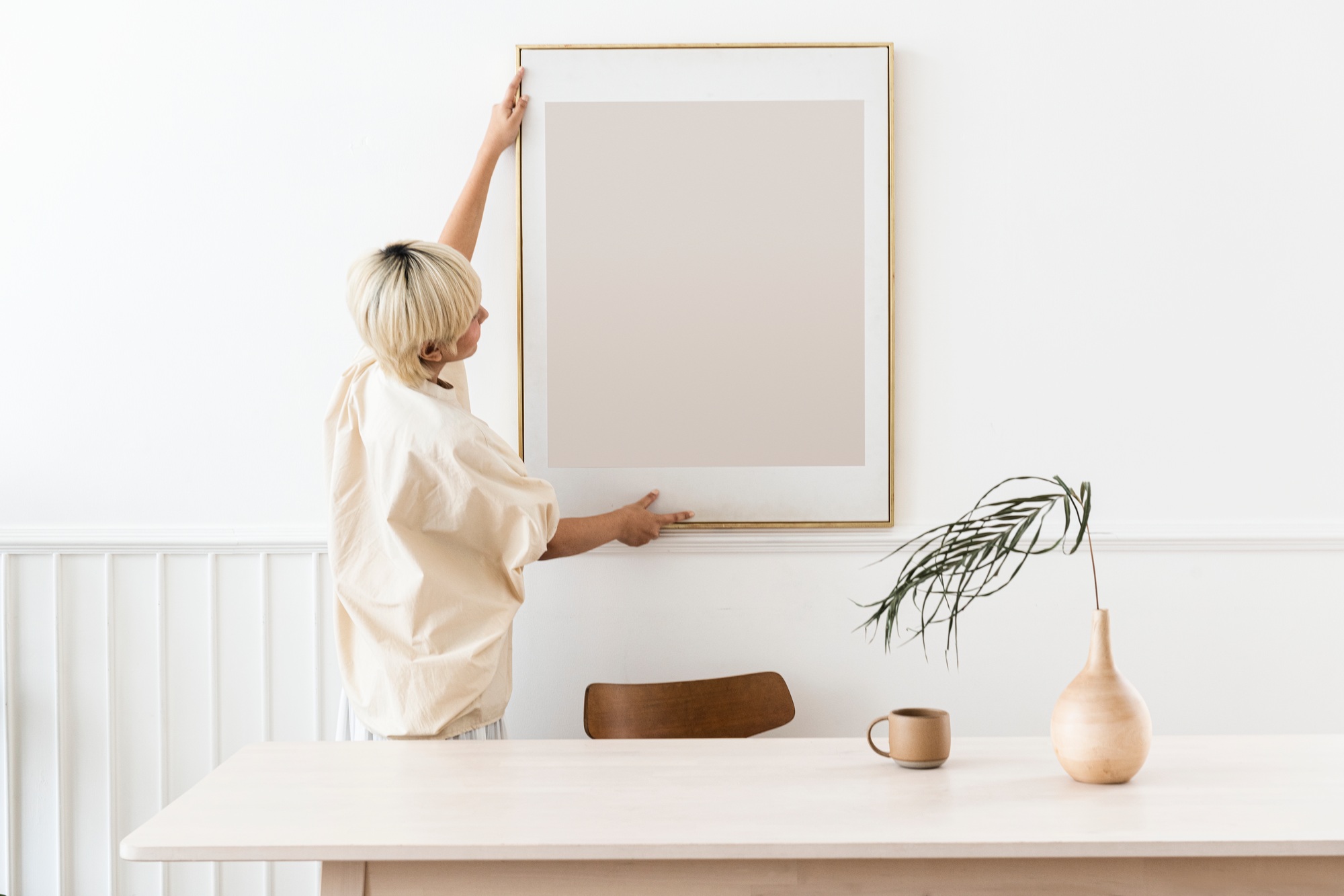 woman hanging a photo frame on a white wall mockup.jpg